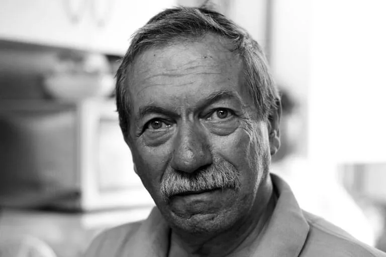 Portrait of an older man with a mustache, wearing a polo shirt, indoors