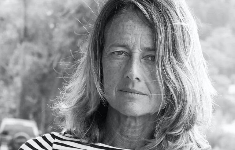 Black and white portrait of a woman with light wavy hair and a striped top, looking directly at the camera with a composed and assured expression.