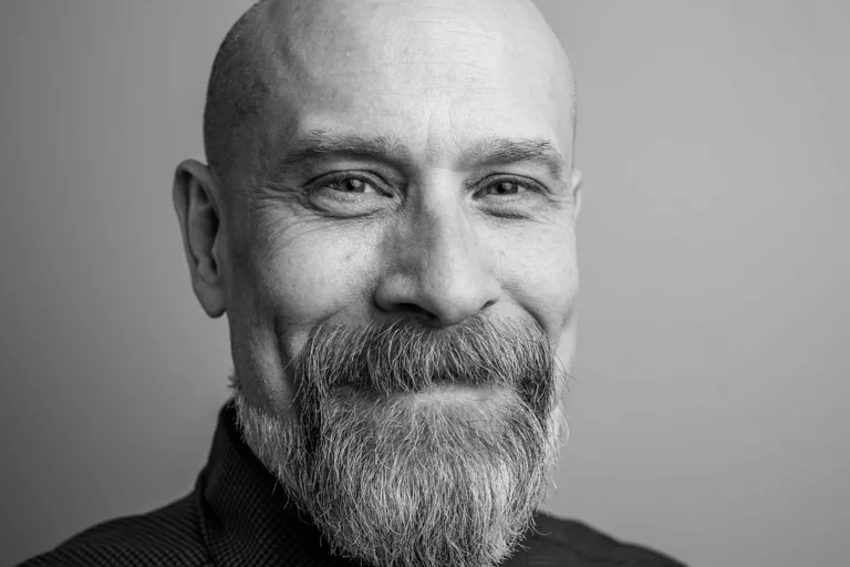 Close-up portrait of a bald man with a grey beard smiling gently