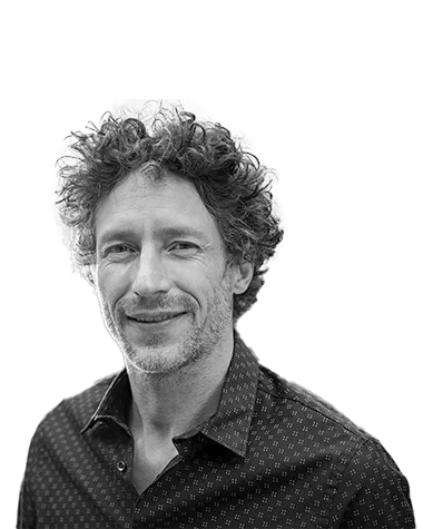 Portrait of a man with curly hair and a patterned shirt, smiling slightly