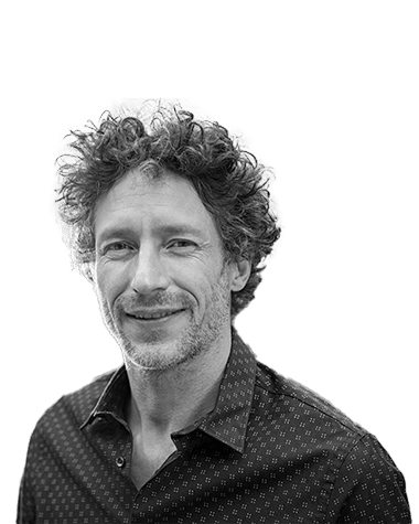 Portrait of a man with curly hair and a patterned shirt, smiling slightly