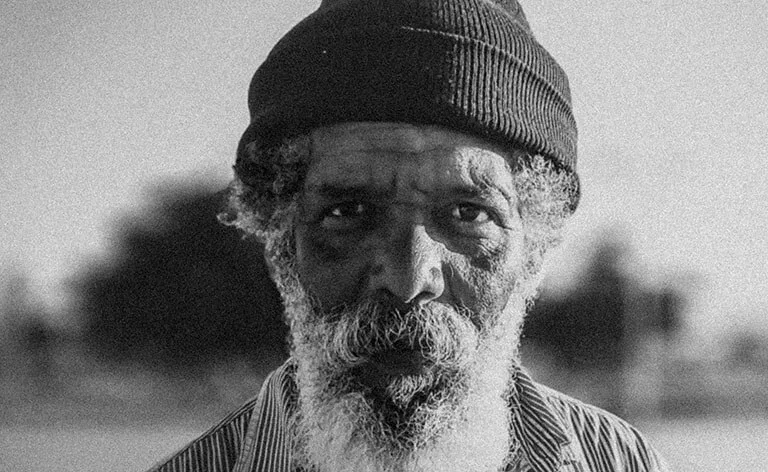 Close-up portrait of an older man with a beanie and a beard, looking straight at the camera