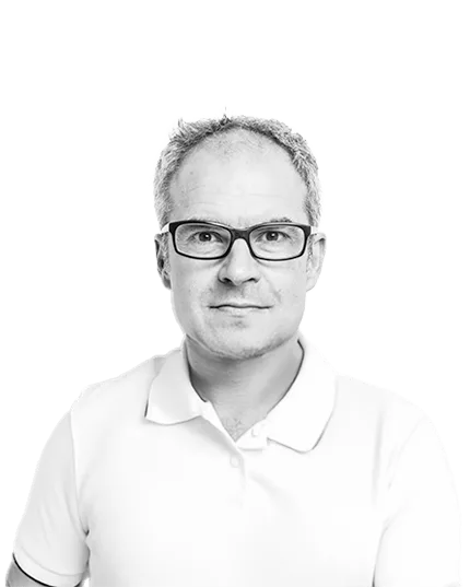 Black and white headshot of a man wearing glasses and a white polo shirt, looking confidently at the camera against a plain light background.