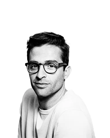 Black and white portrait of a man with short hair and glasses, wearing a light sweater and looking confidently at the camera.