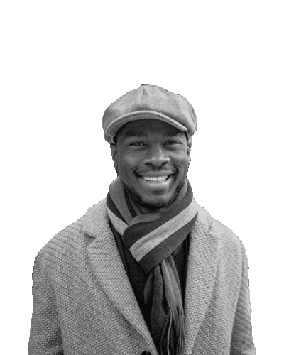 Black and white portrait of a smiling man wearing a flat cap, a warm scarf, and a textured coat, standing against a light background.