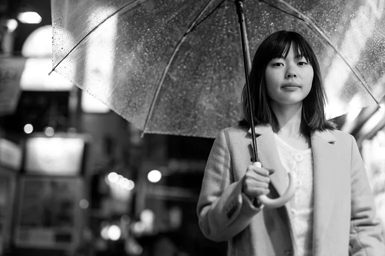 Young woman standing with an umbrella on a rainy night in the city, black and white photo